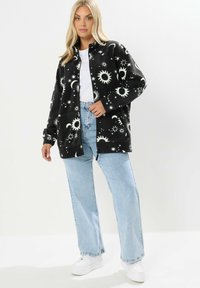 Mustap fleecetakki, jossa on valkoisia taivaankappaleiden kuvioita, kaulusdesign ja etutaskut, yhdistettynä vaaleansinsisiin farkkuihin ja valkoisiin lenkkitossuihin.