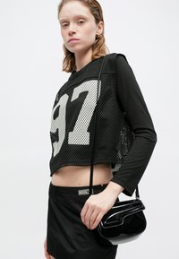 Crni mrežasti crop top s velikim bijelim brojem 97, uparen s crnom mini suknjom. Dodatno ukrašen malom, sjajnom crnom torbicom preko tijela.