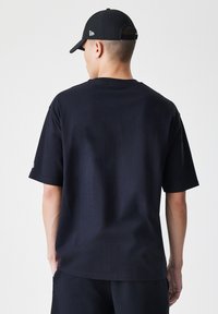 T-shirt in cotone nero con vestibilità rilassata, maniche corte e scollatura rotonda. Il retro presenta un design minimale senza motivi o dettagli visibili.