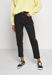 Svarta högmidjade raka jeans med framfickor, bärs med en gul sweatshirt och svarta sneakers. Slät tyg med minimal detaljering.