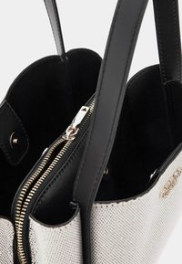 Black and white tote bag with smooth faux leather, textured panel, gold zipper, and interior compartments for organization.