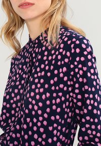 Marinebluse mit pinken Pinselstrichpunkten. Verfügt über einen Stehkragen und eine Knopfleiste, hergestellt aus einem glatten Stoff mit lockerer Passform.