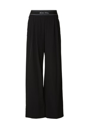 Sorte bukser med vide ben lavet af et blødt stof, med en kontrastfarvet talje med hvide bogstaver og plisseringsdetaljer foran.