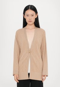 Beige kötött kardigán nyitott elülső résszel, széles ujjakkal, gyémántmintával és egy gombos záródással. Puha tapintású, laza fazonú.