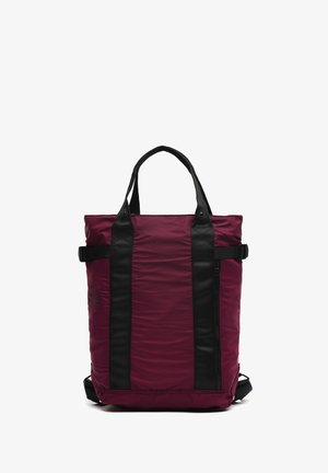 Raudonai ir juodai dryžuota rankinė, pagaminta iš tvirtos medžiagos, turi dvi rankenas, reguliuojamas juostas, šoninį užtrauktuką ir glotnią tekstūrą.