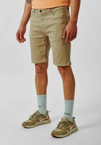 Beige katoenen shorts met een rechte pasvorm en voorzakken, gecombineerd met lichtblauwe sokken en beige sneakers met een subtiel ontwerp.