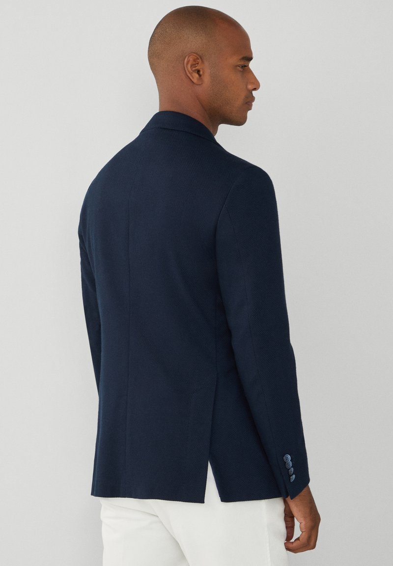 Blazer navy con acabado texturizado, con una abertura en la parte trasera y detalles de botones en las mangas. Ajuste entallado con un diseño clásico.