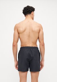 Shorts de bain noirs avec une taille élastique, une poche arrière et un matériau lisse et léger. Sans motifs ni accents supplémentaires visibles.