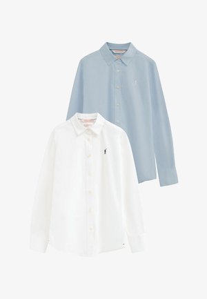 Dos camisas de manga larga con botones, una blanca con logo negro y otra azul claro con logo blanco, ambas con cuellos puntiagudos.
