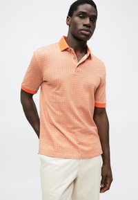 Polo cu mânecă scurtă, de culoare portocalie, cu un model geometric. Prezintă un guler portocaliu în contrast și o plachetă de nasturi. Textură fină.