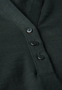 Cardigan verde scuro con colletto a V, caratterizzato da tre bottoni neri e una trama a coste. La vista ravvicinata evidenzia i dettagli dei bottoni.