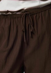 Pantalon marron avec cordon et taille élastique porté avec un haut rayé blanc et rose.
