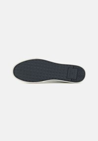 Suela de zapato de goma negra con un patrón de diamantes, borde exterior blanco y logotipo grabado. Textura suave con un diseño claro y sólido.