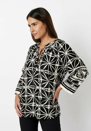 Schwarz-weiße gemusterte Bluse mit einem gebundenen Ausschnitt, Dreiviertelärmeln und einer lockeren Passform. Sie hat geometrische Designs und kontrastierende Akzente.
