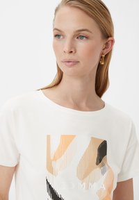 Weißes Baumwoll-T-Shirt mit einem abstrakten Design in Orange, Beige und Schwarz. Kurze Ärmel, runder Halsausschnitt und dezentes "COMMA"-Printdetail.
