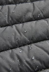 Gros plan de gouttelettes d'eau perlant sur un tissu imperméable matelassé gris foncé, montrant la résistance à l'humidité et les détails de la texture.