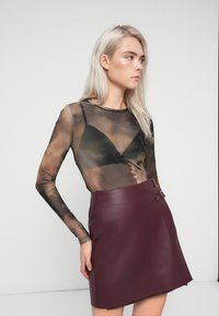 Διαφανής μπλούζα με μακριά μανίκια, από κάτω φορεμένη με μαύρο τριγωνικό σουτιέν, συνδυασμένη με εφαρμοστό μπορντό σατέν φούστα που διαθέτει ασημένιες λεπτομέρειες.