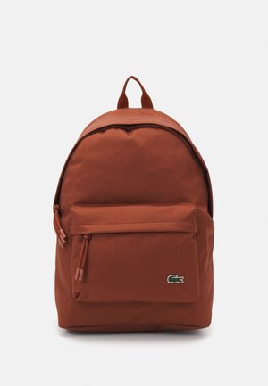 Batoh barvy rzi s přední kapsou na zip a malým zeleným logem krokodýla v dolní pravé části, na jednobarevném světlém pozadí.