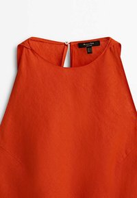 Rdzawooncza, bezrękawnikowa bluzka wykonana z teksturowanej tkaniny, z okrągłym dekoltem i zapięciem na guzik z tyłu.