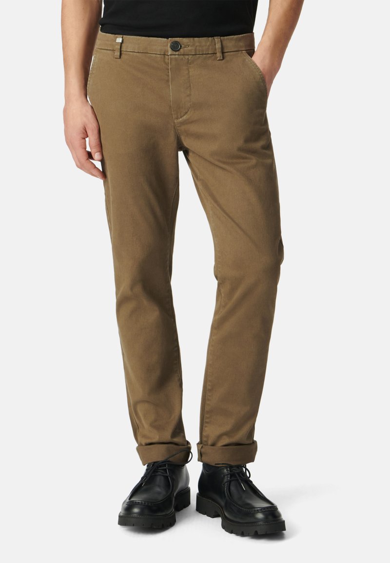 Bruine chino's met een rechte pasvorm, voorzien van een knoopsluiting, zijzakken en opgerolde mouwen, gecombineerd met zwarte veterschoenen.