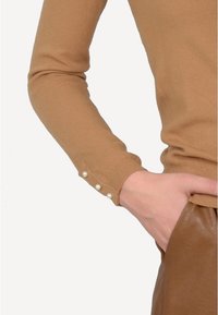 Bruine gebreide trui met lange mouwen, voorzien van drie parelaccenten op de manchetten. Soepele textuur en een aansluitend ontwerp.