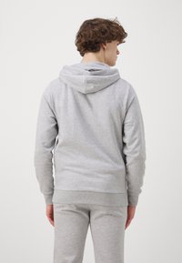 Haut en coton gris clair avec capuche à cordon de serrage, poignets et taille côtelés, associé à un pantalon gris assorti. Design simple et décontracté.