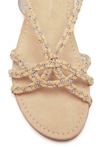 Sandalias trenzadas de color marrón claro con un diseño de tiras texturizadas, adornadas con acentos metálicos. Suela plana con un acabado suave.