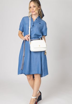 Abito camicia in denim con maniche corte, chiusura frontale a bottoni e cintura. Abbinato a una borsa a tracolla bianca e sandali con zeppa.