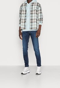 Rutig flanellskjorta i ljusblått, grått och svart över en ljusblå hoodie. Tillsammans med mörka jeans och vita högklassiga sneakers.