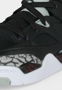 Μαύρο αθλητικό παπούτσι με παχιά μαύρα κορδόνια, σπασμένη γκρί και μαύρη με σχέδιο ενδιάμεση σόλα και λευκή υφή σόλα με κόκκινες κηλίδες.