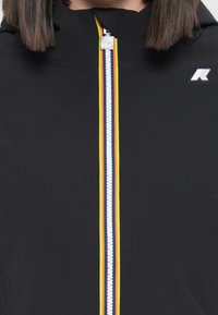 Giacca nera con cerniera frontale, caratterizzata da strisce colorate (giallo, arancione, blu) e un marchio vicino al colletto.