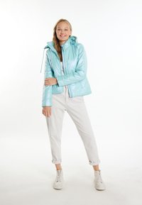 Giacca imbottita azzurra chiara con cappuccio, con una finitura lucida, motivo a quadri diagonali e zip frontale. Abbinata a pantaloni bianchi e scarpe da ginnastica.