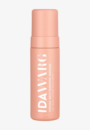 Zelfbruinende mousse in een hoge, cilindervormige, matte perzikkleurige fles met een brede witte label en dop, met gedurfde tekst en geurspecificaties.