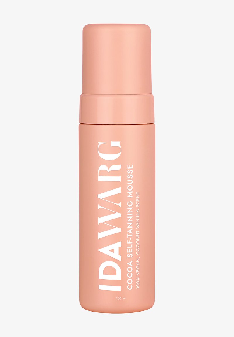 Mousse autobronzante dans une bouteille haute et cylindrique, en finition mate pêche, avec une large étiquette et un capuchon blancs, présentant un texte en gras et des détails sur le parfum.