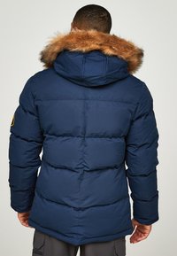 Tumši zila pūka jaka ar vilnas oderi kapuce, ar kvadrātu rakstu un logotipa uzšuvumu uz kreisā piedurkne.