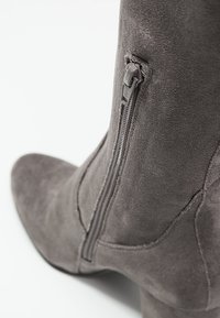Stivale ankle in suede grigio con punta appuntita e dettaglio della zip laterale. Caratterizzato da una texture liscia e una silhouette strutturata.