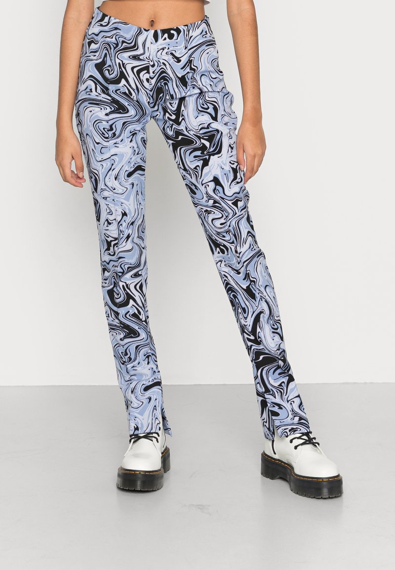 Calças em azul e preto com padrão mármore, de corte slim e textura suave, combinadas com sapatos brancos de plataforma grossa.