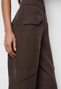 Braune Cargo-Hose mit glatter Textur, elastischem Bund und zwei vorderen Taschen mit schrägen Klappen. Für Funktionalität entworfen.