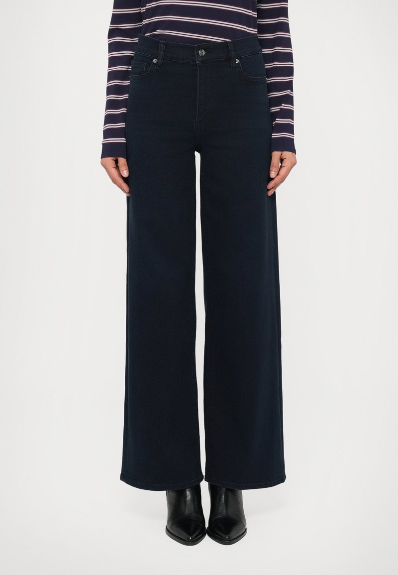 Laiade lahjaga tume teksapüksid kõrge vöökohaga, millel ees nupu sulgemine ja neli klassikalist taskut. Sile tekstuur; nähtavaid mustreid pole.