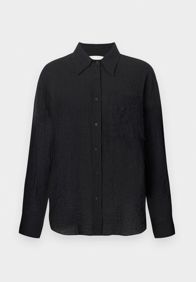 Mustan värvi nööbiga särk, millel on tekstuurne muster, terav krae, pikad varrukad ja rinnatasku. Valmistatud kergest kangast.