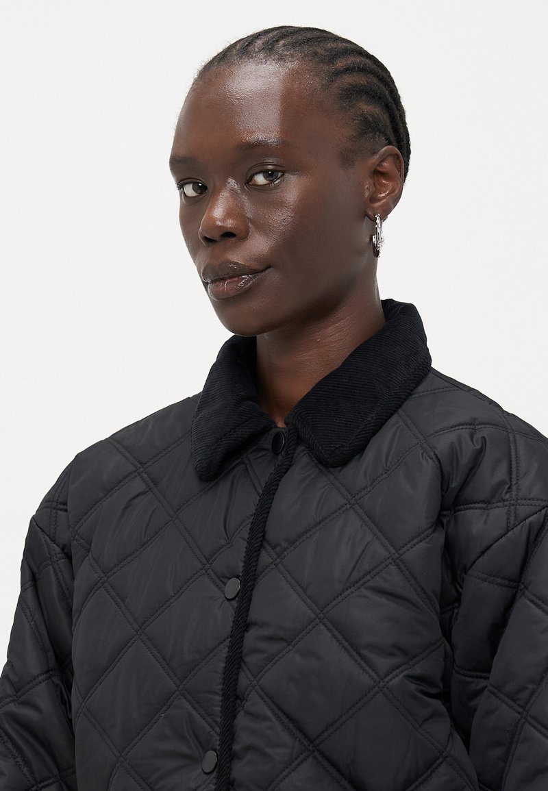 Veste matelassée noire avec un col en velours côtelé, présentant des motifs en losange et une fermeture à boutons-pression ; texture lisse et design moderne.