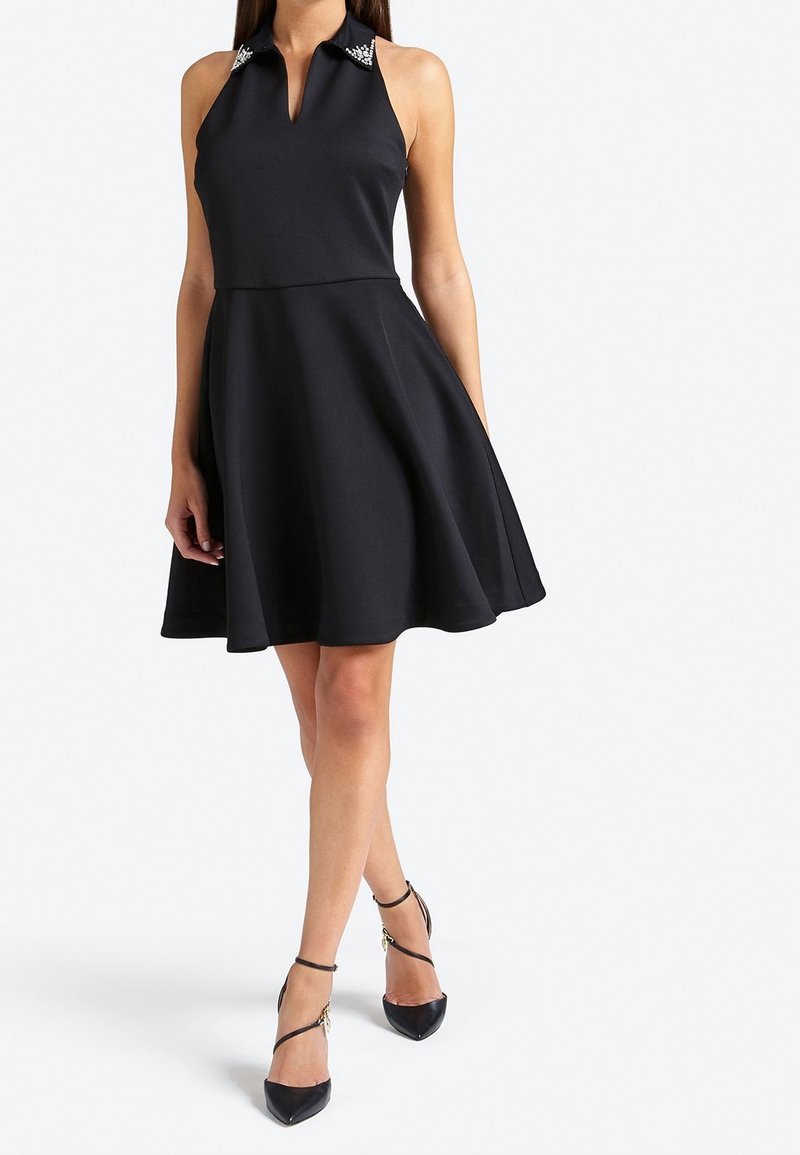 Robe noire à encolure halter avec un corsage ajusté et une jupe évasée, mettant en avant des détails de col embellis et une texture de tissu lisse.