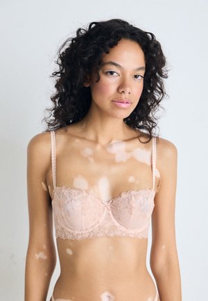 Lace beha in zachtroze met geborduurde bloemenpatronen, semi-doorzichtige cups, verstelbare bandjes en een delicaat strikje in het midden.