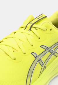 Baskets de sport jaunes vives avec une tige texturée, des lacets plats et un logo ASICS argenté sur le côté, avec un col et une languette rembourrés.