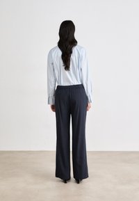 Camisa azul claro com botão e mangas compridas. Calças largas em azul marinho com cintura elástica. Texturas suaves e design simples.