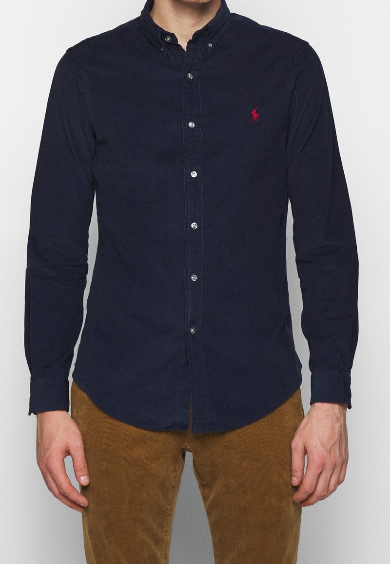 Granatowa koszula na guziki wykonana z mieszanki bawełny, z klasycznym kołnierzykiem, długim rękawem oraz małym czerwonym logo na lewej piersi.
