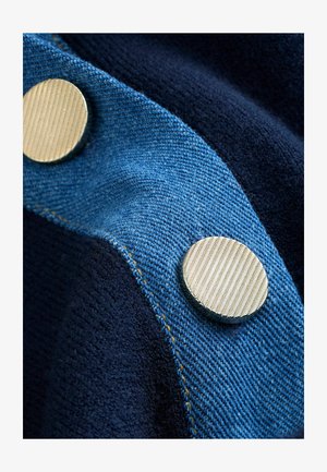 Denim fabric in blue with a textured surface, paired with a navy wool blend. Features two shiny, round metal buttons.
