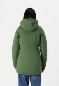 Zeleni puffer jacket s kapuljačom, teksturirani materijal, strukirana linija te bočni gumbi. Ima malo duži stražnji dio za dodatnu zaštitu.