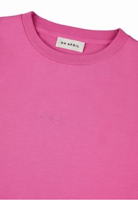 Rozā T-krekls ar apaļu kakla izgriezumu, mīksta tekstūra un smalka izšūta logo gaišākā tonī. Gluda auduma virsma bez redzamām šuvēm.