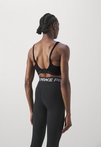 Svart sports-BH med justerbare stropper og kroklukking, kombinert med høytaljede svarte tights med en merkevarebelte.